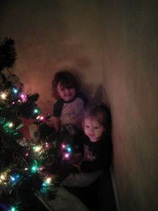 Two of Sonja and my grands hanging out behind our Christmas tree: Rory & Annie God help us to pass on the message behind the tree!
